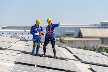 Two solar panel engineers in safety gear inspect the installation on a factory rooftop