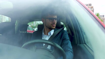 Serious young confident man in glasses driving car in the city while looking around. Transport, business and people concept. Real time