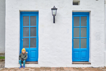 Latin child sitting in front of a light blue door in a house at Tucuman, Argentina. Winter vacations