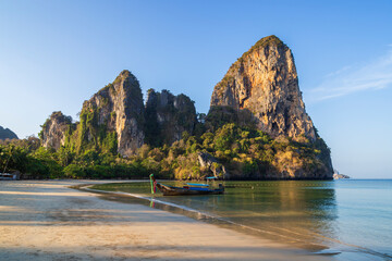Scenic view of a long-tail boat at the empty Railay West beach and high limestone cliffs in Railay,...
