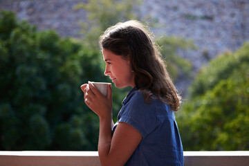Profile, woman and thinking with coffee by balcony in house, apartment and home for nutrition, drink and wellness. Vision, calm and happiness for tea, espresso and breakfast outdoor by trees in Peru