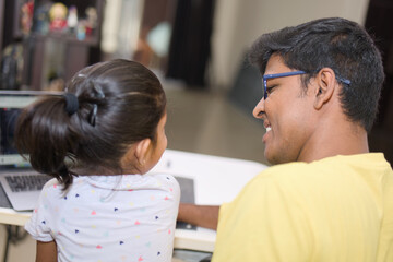 Back view of father and daughter looking at computer monitor in living room at home