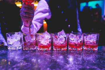 Bartender working, beautiful row line of different coloured liquor alcohol cocktails on a party in...