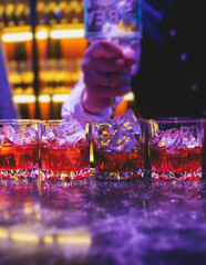 Bartender working, beautiful row line of different coloured liquor alcohol cocktails on a party in a bar, and others on catering banquet on event, barman mixing drinks and beverages in a club
