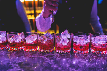 Bartender working, beautiful row line of different coloured liquor alcohol cocktails on a party in...