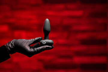 Silicone anal plug in a female hand in black latex gloves on a black background. Massager with...