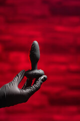 Silicone anal plug in a female hand in black latex gloves on a black background. Massager with...