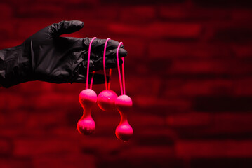 Obraz premium Woman's hand in black latex gloves holds pink Kegel balls and Ben Wa balls on a red background. Vaginal balls in a woman's hand. Sex toys Geisha Balls, Products for intimate stores