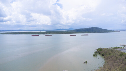 Coal barges lined up in the Kalimantan sea with mountains and clouds in the background