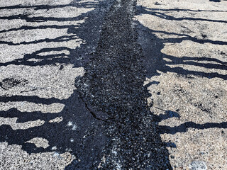 Asphalt on road. Street with black tar filling the cracks. Cracks in concrete surface are then...