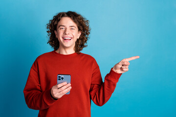 Photo of cheerful positive guy dressed red pullover texting modern gadget pointing emtpy space...