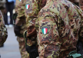 Platoon of Italian soldiers in camouflage uniforms standing at attention with with flag emblem on...