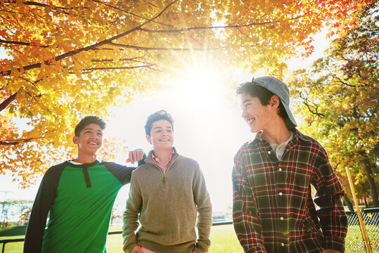 Happy, boys or friends in park together for fall holiday, break or trust and support. Smiling, young men or group of teenagers walking in forest for talking, connection and outdoor adventure