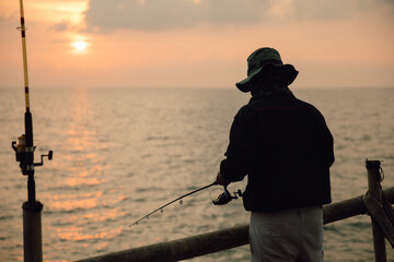 Fishing at sunset Silhouette of a man with a fishing pole by the sea