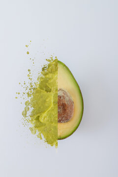 One half avocato showing the fruit and one half of guacamole splatter texture