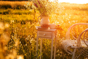 vintage white armchair and table with a cup of tea in a field at sunset. soft sunlight. tea party...