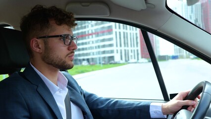 Calm young man in glasses driving along the street on the car and looking at the road. Side view. Transport, business and people concept. Real time
