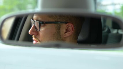 Young male face reflected in car mirror. Man in glasses driving car in the city. Transport, business, lifestyle and people concept. Real time