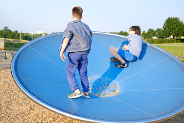 two boys, children 9-10 years play in playground, try to keep balance on balance wheel, fun piece...