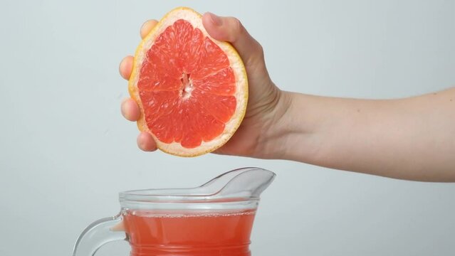 Hand squeezing grapefruit juice from half a grapefruit on a white background.
