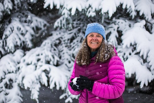 A portrait of a happy middle aged woman holding a snow ball on cold and snowy day in Colorado, USA