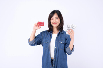 Asian woman wearing denim jean is holding dollar and credit card against a white background,...