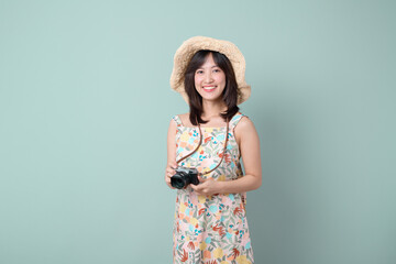 Happy Asian woman wearing casual dress and hat with camera on vacation or travel theme isolated on pastel green background. Travel and vacation concept.