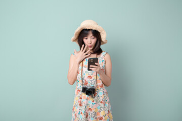 Happy Asian woman wearing casual dress and hat with camera while getting amazing news on mobile...