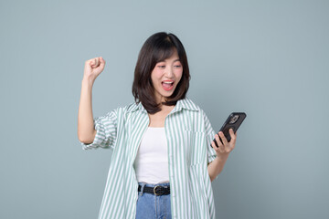 Happy asian woman do winner dance, triumphing, winning on mobile phone video game, holding smartphone horizontal position and celebrating, green background