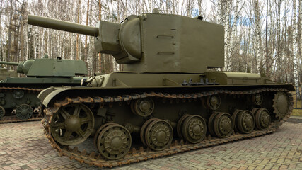 A large green tank with a black barrel sits in front of a forest