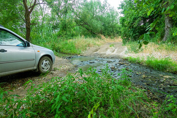 A passenger car crosses a forest stream on a muddy road