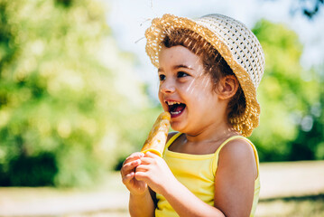 Cute happy little girl in yellow dress eating fruit ice cream. Summer fun child play in park. Summertime vibrant color background.
