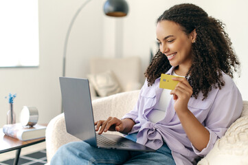 Positive hispanic or brazilian curly haired woman customer shopper using credit card and laptop to...