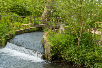 water cascading over a small weir in the river with an old wooden bridge in the background