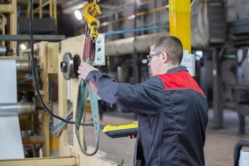A worker at a factory turns on the installation of an overhead crane to lift a load.
