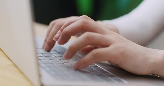 Camera view of positive Asian woman sitting at table and working on her portative laptop at home or office. Pretty female typing text on keyboard or mailing with someone on digital device.