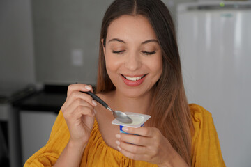 Hispanic cheerful young woman eating yogurt natural in the kitchen at home