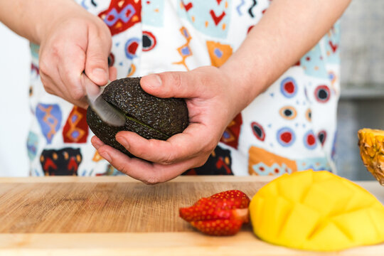 Young man cutting avocado while standing in kitchen at home