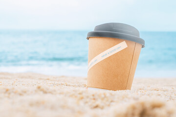 A paper cup with coffee on the sand by the sea. The concept of a morning coffee with the...