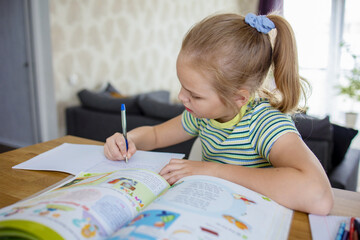 A pretty little student does her homework based on a textbook and makes notes in a workbook. The...