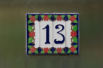 Vintage house number 13 in earthenware on the entrance of a painted wall