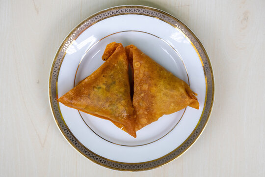 Two samosas on a white plate. Asian delicious food. It is known as sambusa, singara, samose, somsa, singada, and samuza. Top view