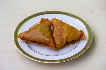 Two samosas on a white plate. Asian delicious food with a savory filling, including ingredients such as spiced potatoes, onions, peas, meat, or fish. 