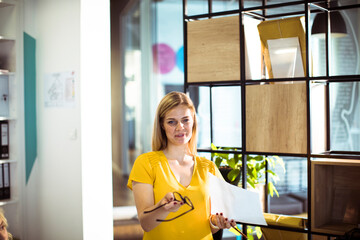 Office workers in a meeting with one woman standing and holding paperwork