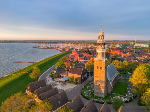 Aerial drone image of historic small city of Hindeloopen, Hylpen with dike, marina, seawall, next to IJsselmeer lake with iconic church and village during spectacular sunset