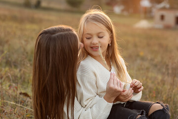 Family day, mother's day. Happy smiling young mom and adorable child daughter soft hugging, kissing and spending time together at autumn on sunset. Idyllic family having fun outdoors on fall holiday.