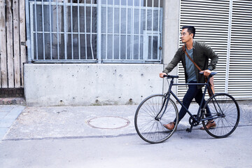 Fototapeta premium Travel, street and man with bicycle in city commuting to work for creative career. Transport, road and male designer with carbon footprint for cycling to office with bike in town in Amsterdam.