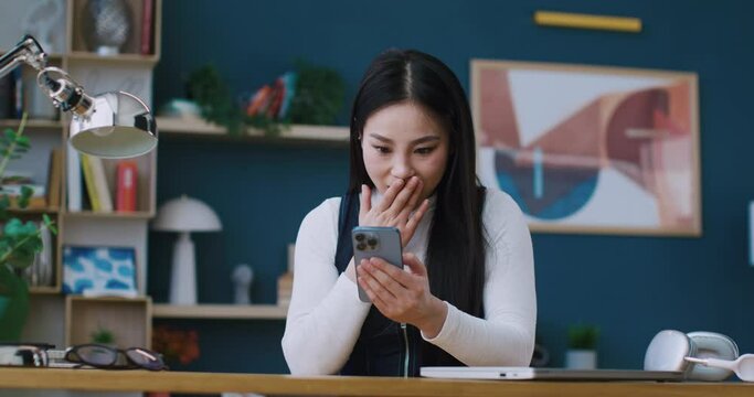 Young Chinese student celebrating successful passing of exam. Joyful girl using phone while checking her grades for her studies. Concept of victory and success. Feeling excited of getting good news.