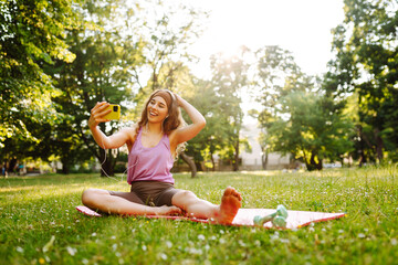 Sportswoman in sportswear chooses or listens to music during training while sits on the mat...