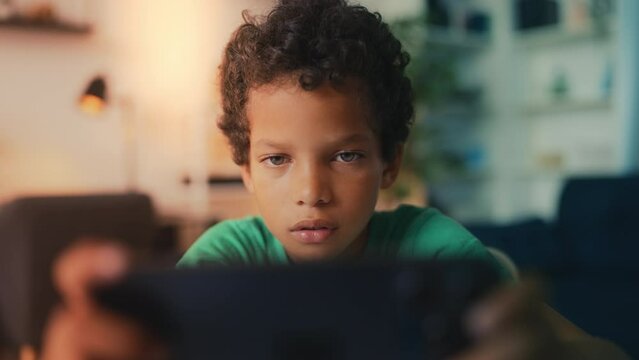 Little African American boy uses smartphone for games instead of studying